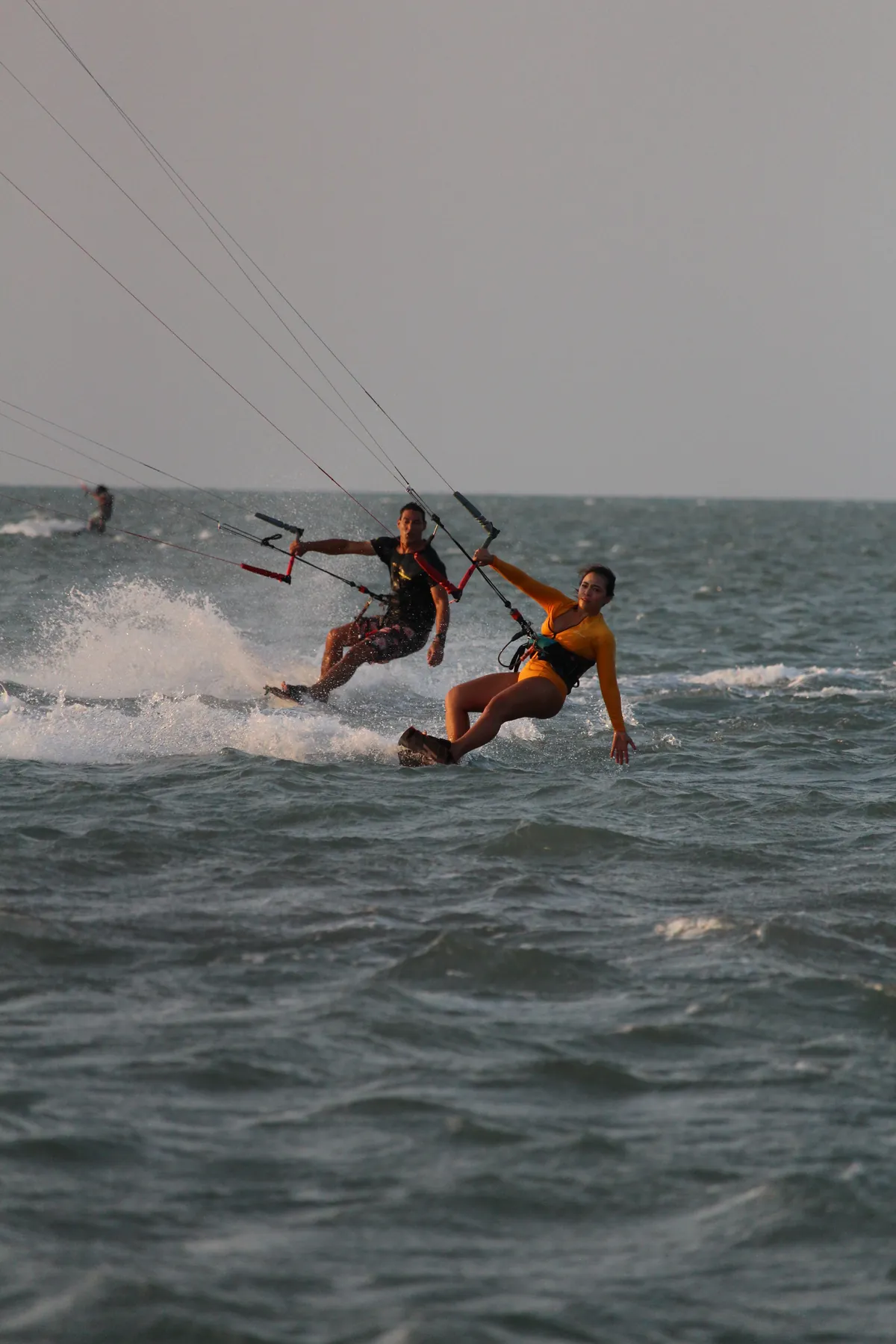 Kitesurfistas navegando nas águas rasas da Ilha do Guajirú ao entardecer com spray de água ao redor