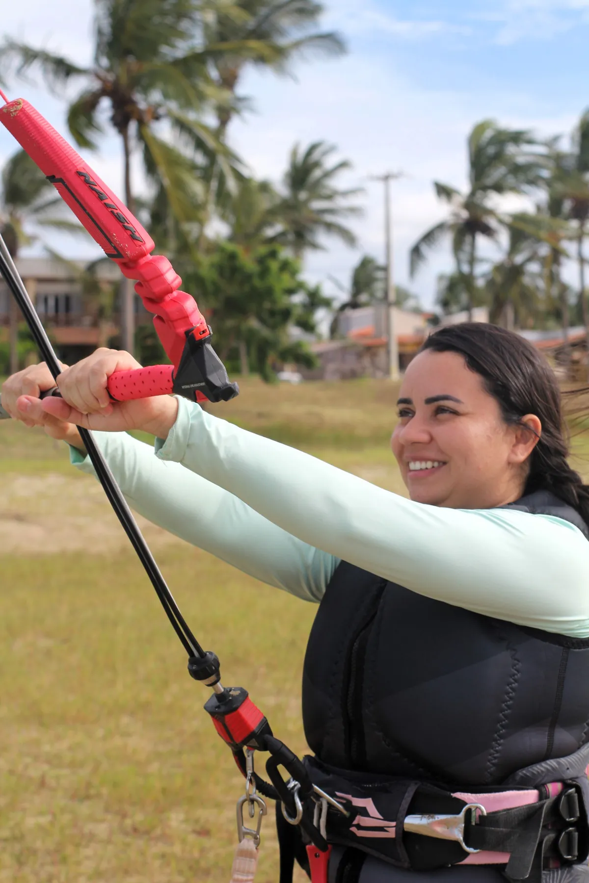 Instrutora segurando barra de kite e sorrindo durante aula em dia ensolarado na Ilha do Guajirú com coqueiros ao fundo