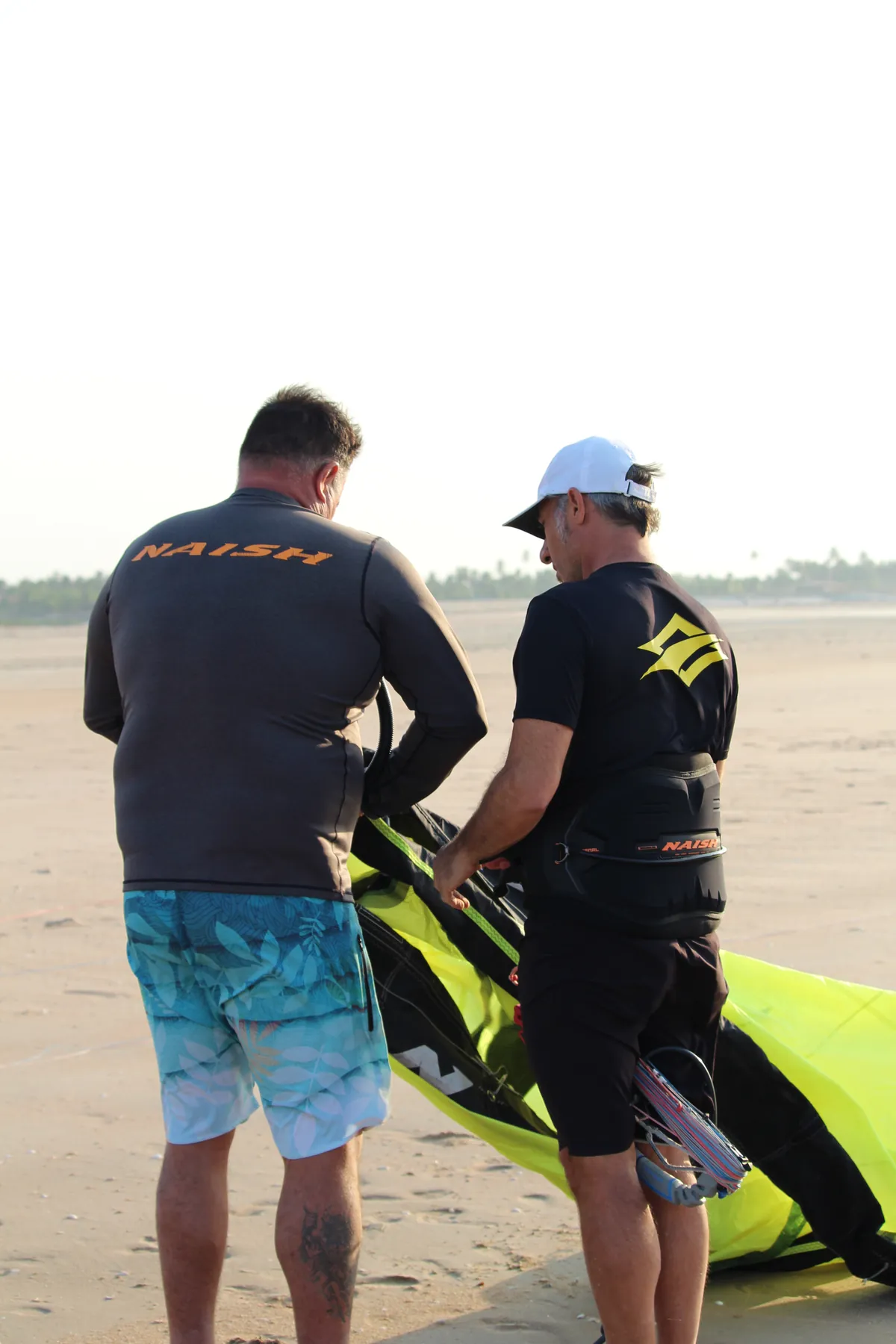 Two instructors with blue and green kites talking on the beach at Ilha do Guajirú