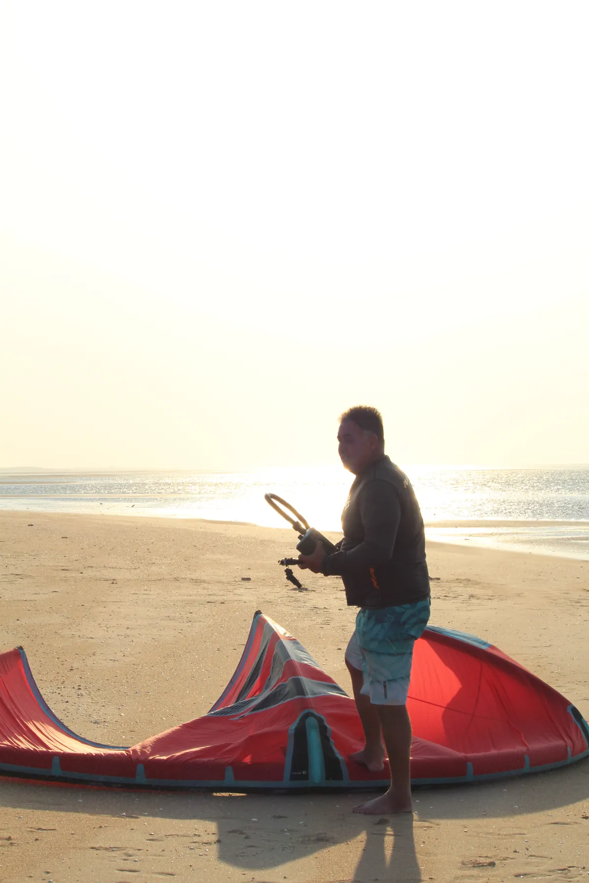 Instructor preparing a red kite on the beach at Ilha do Guajirú at dusk