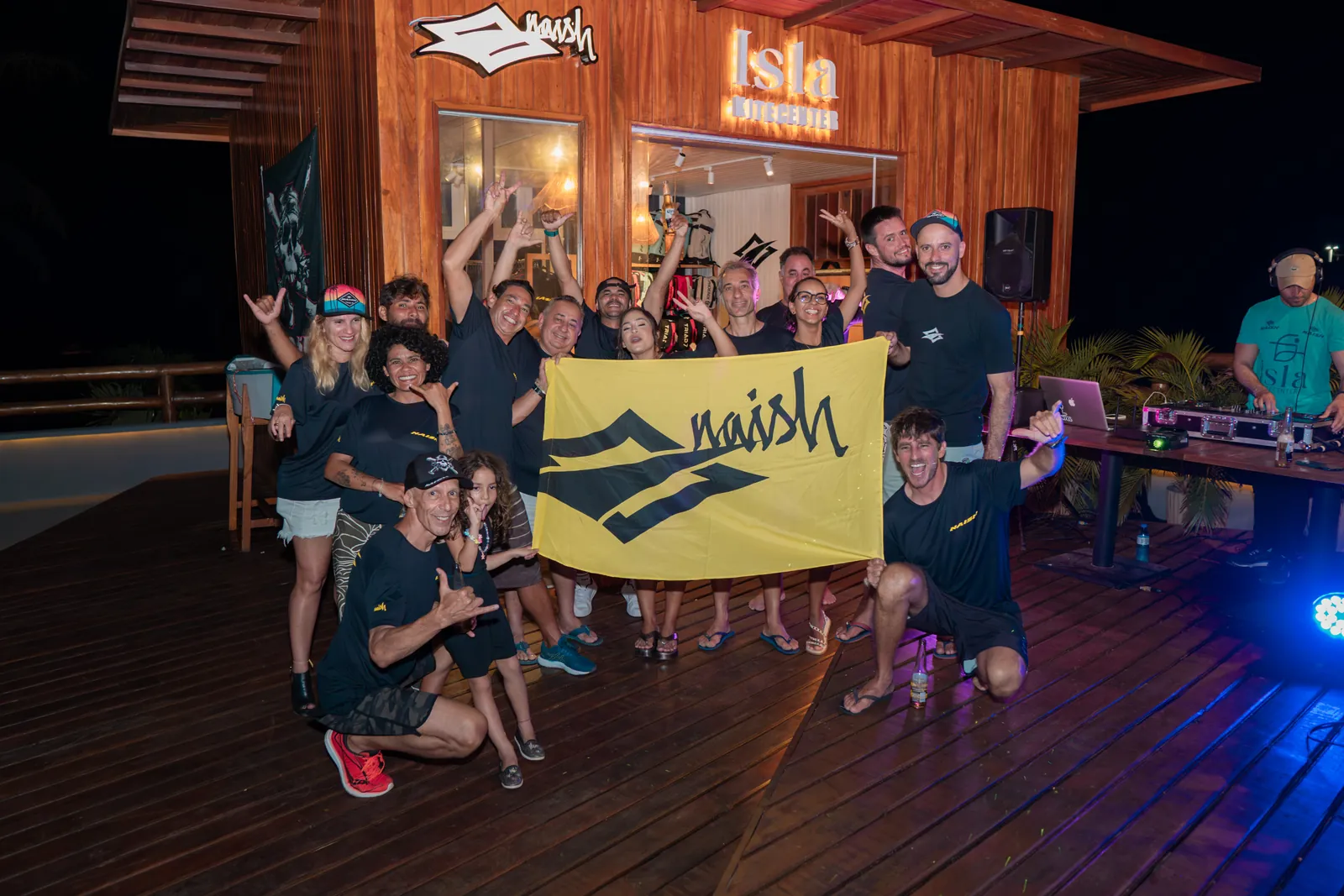 Grupo de alunos e equipe posando com bandeira Naish dentro da escola Isla Kite Center na Ilha do Guajirú