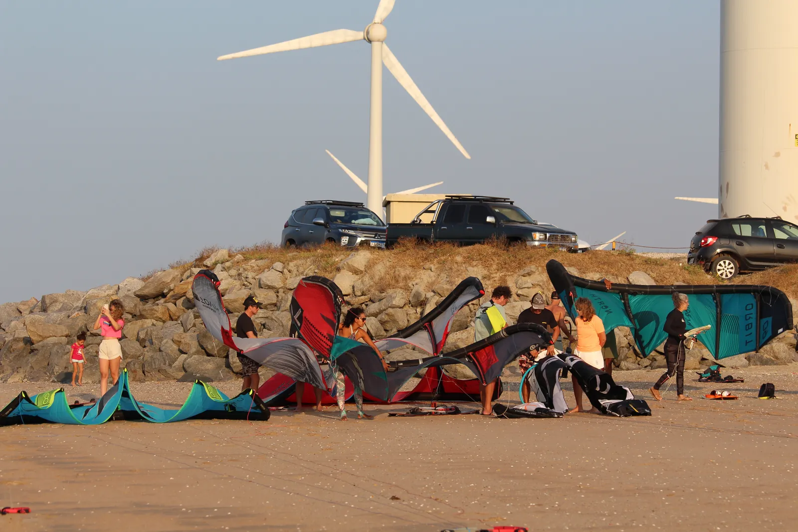 Vista da praia da Ilha do Guajirú com kitesurfistas e equipamentos espalhados na areia ao fundo