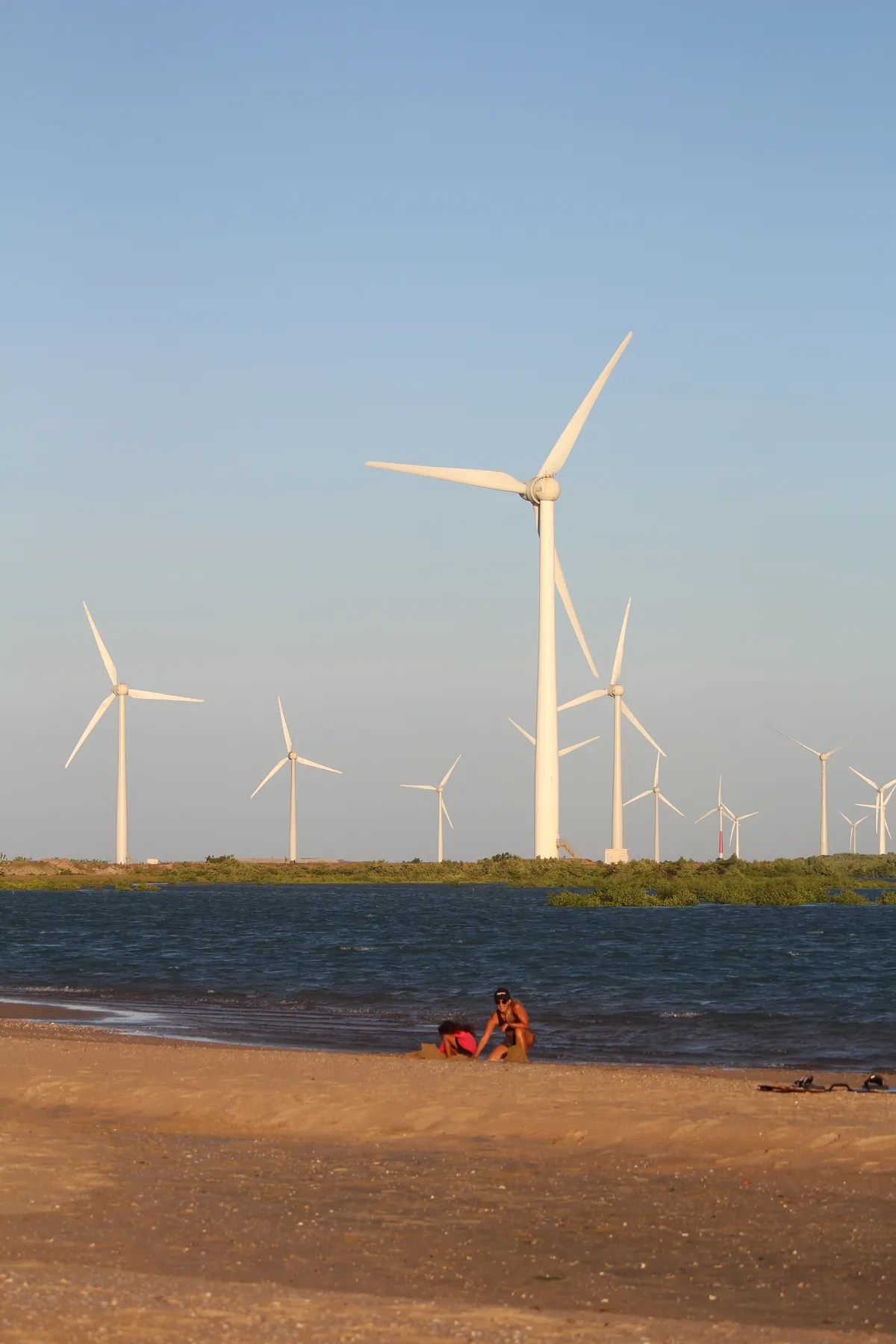 Praia da Ilha do Guajirú com aerogeradores ao fundo e equipamento de kitesurf na areia